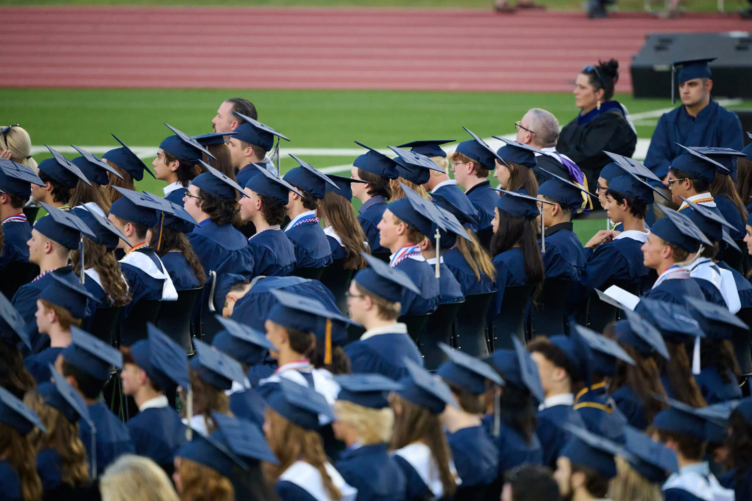 Graduates seated in caps and gowns at an outdoor commencement ceremony.