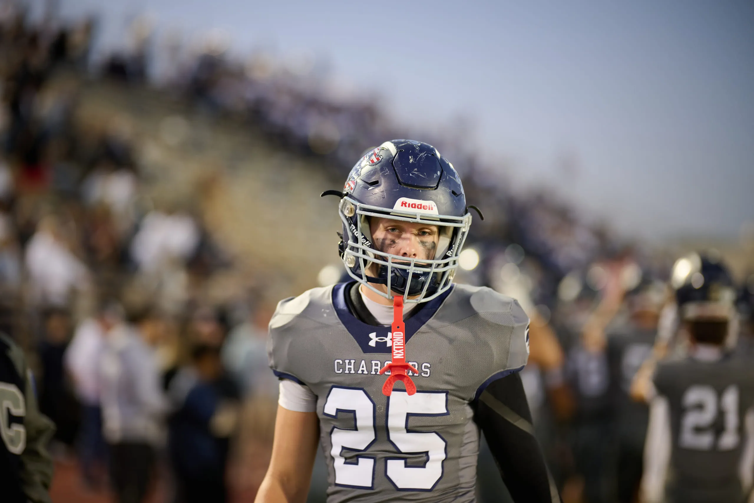 A high school football player on the sideline under stadium lights, packed home stands behind him.