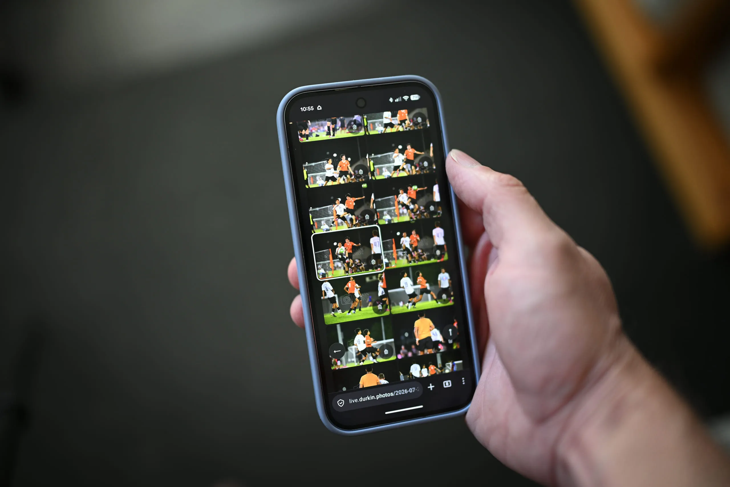 A hand holding a phone displaying a grid of football photos in a live event gallery