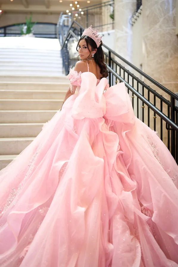 A quinceañera in a pink ball gown and tiara on a staircase